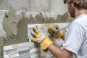 Man pressing an ornamental tile into a glue on a wall with gloved hands in a DIY concept.